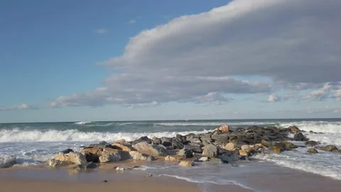 Stone breakwaters. sandy beach. blue sky. Large sea waves with white foam Stock Footage 144108492