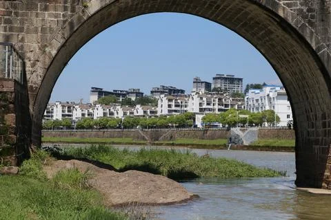 Stone bridge arch frames a riverside city view with white buildings and bro.. Stock Photos
