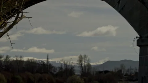 Stone bridge arch framing a scenic landscape with snow capped mountains Stock Footage 335461804