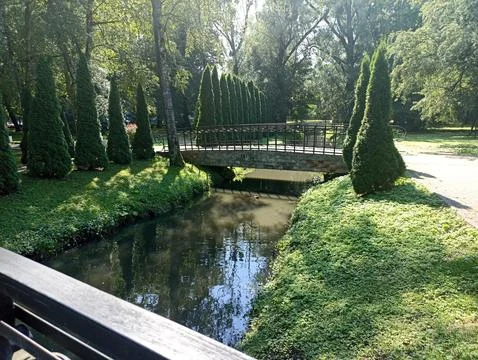 A stone bridge crossing a small river, surrounded by green trees and lush Stock Photos