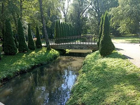A stone bridge crossing a small river, surrounded by green trees and lush Stock Photos
