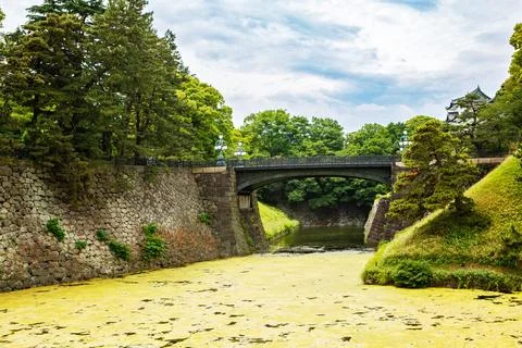 Stone bridge over moat with historic palace building and lush trees in Toky.. Stock Photos