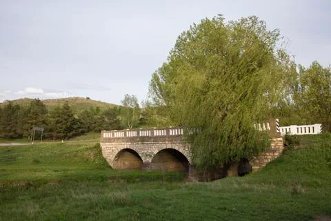 A stone bridge over a small river flowing in country. Stock Photos