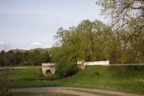 A stone bridge over a small river flowing in country. Stock Photos