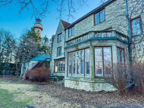 A stone building stands with large windows. Trees surround the area, and a ta Foto stock