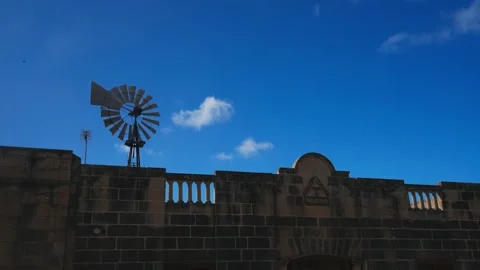 Stone Building with Windmill Against Clear Blue Sky and Scattered Clouds Stock Footage 340555927