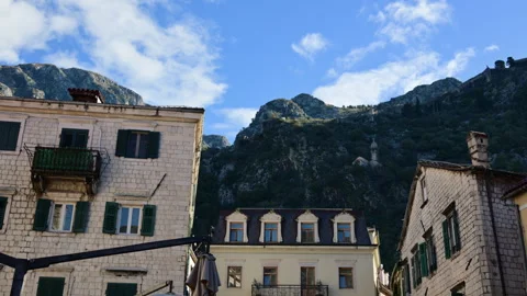 Stone buildings with shutters standing in front of rugged bay mountains under a Stock Footage 329320435