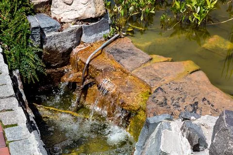 Stone cascading waterfall in an artificial pond with water in the park. Stock Photos