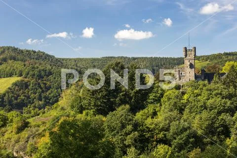 Stone castle turret on top of rolling treed hills with blue sky and clouds Stock Photos