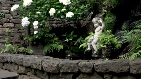 Stone cherub statue sitting on edge of garden pond Видео 293158918