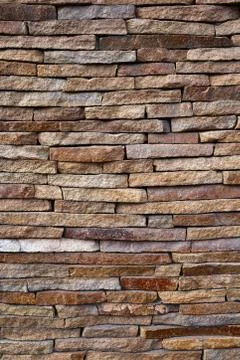 Stone cladding wall made of striped stacked slabs of natural brown rocks. Stock Photos