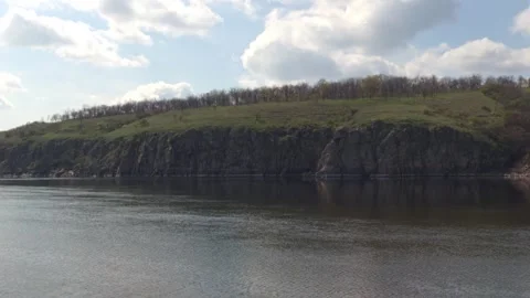 Stone cliffs above a river with spring greenery on the slopes and cloudy sky Stock Footage 332735392