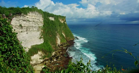 Stone cliffs are immersed in tropical greenery and blue ocean waves foaming on Video stock 227002855