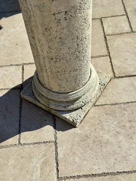 Stone column with square base on tile floor, sunlight Stock Photos