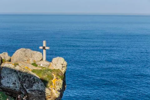 Stone cross on the edge of a cliff overlooking the ocean Stock Photos