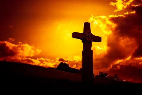 A stone cross in front of a dramatic evening sky Stock Photos