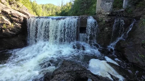 Stone dam waterfall plunging into fast river between rugged green cliffs Video stock 344058835