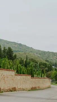 Stone fence with red tile capping along a quiet road against a green hillside Stock Photos