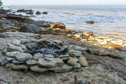 Stone fire pit on rocky Baltic Sea shore with calm evening water Foto stock