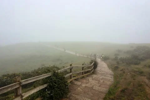 A stone footpath leads down through a wooden fence along a misty green hillsi Stock Photos