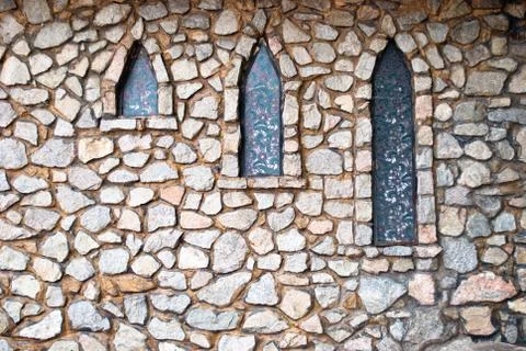 Stone gray wall with three narrow windows in the shade of trees Stock Photos