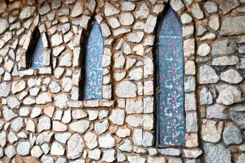 Stone gray wall with three narrow windows in the shade of trees Stock Photos