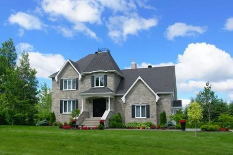 Stone house exterior with red flowers and green grass and trees Stock Photos