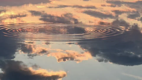 Stone impact ripples distorting reflected sunset clouds in lake, slow motion Stock Footage 338238177