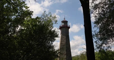 Stone lighthouse framed by trees under blue sky and summer clouds Stock Footage 320017676