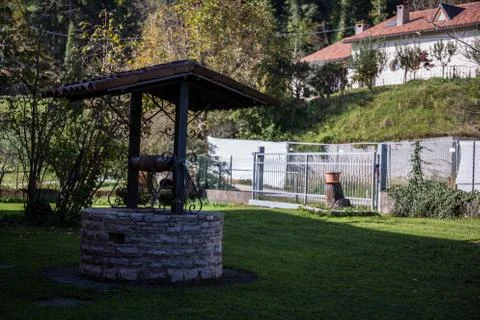 Stone old well standing on the grass in a garden  in the shadow Stock Photos