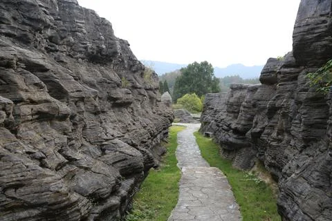 Stone path cutting through tall walls of layered dark rock Foto stock