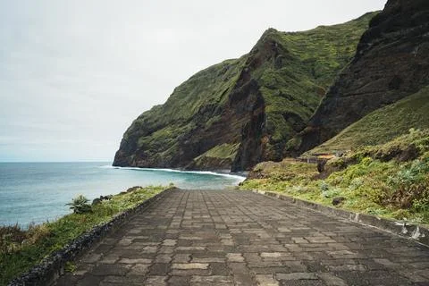 Stone path descends to the ocean shore with lush green mountains under a di.. Stock Photos