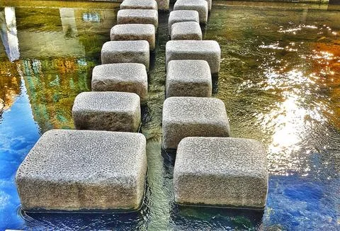 Stone path over gently flowing water creates a peaceful scene with sunlit ref Stock Photos