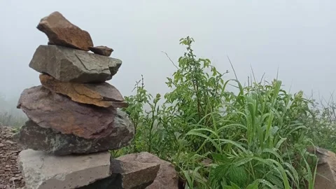 A stone pyramid on the edge of a cliff and green grass with dew drops Stock Footage 246652024