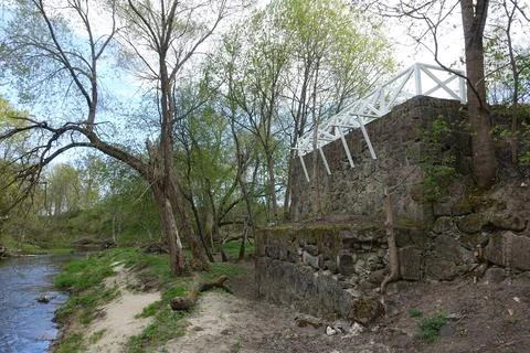 Stone remnants of an old structure border a tranquil river amidst vibrant gre Stock Photos