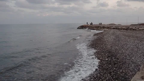 A stone shore against the background of which fishermen cast their fishing rods. Stock Footage 260209101