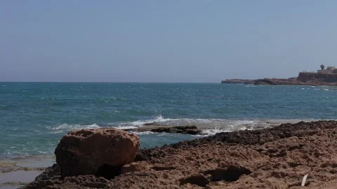 Stone shore and blue water, waves hitting and splashing foam. Filmed in slo.. Video stock 280257597