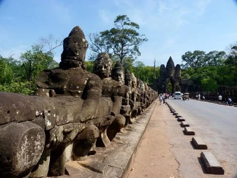 Stone statues before gate of Angkor Thom with street, ruins of Angkor, Cambodia Stock Photos