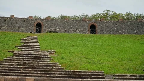 Stone steps and grassy arena inside the Pompeii Amphitheatre, with arched Видео 336214630
