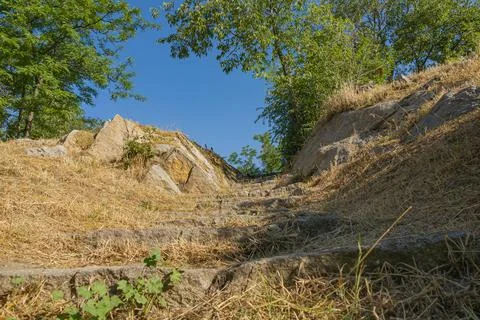 Stone steps climbing a dry hillside between rocks and trees under clear blu.. Stock-Fotos