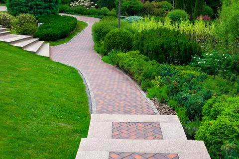 Stone steps descent to a path from paving slabs in a park on a slope. Stock Photos