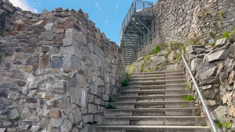Stone steps lead up to ancient ruins with rugged rock walls and a modern metal Stockbeeldmateriaal 297758941