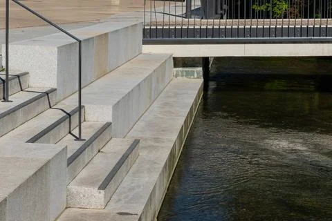 Stone steps leading down to a calm river near a pedestrian bridge Stock Photos