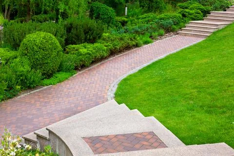 Stone steps to a path from paving slabs in a park on a slope. Stock Photos