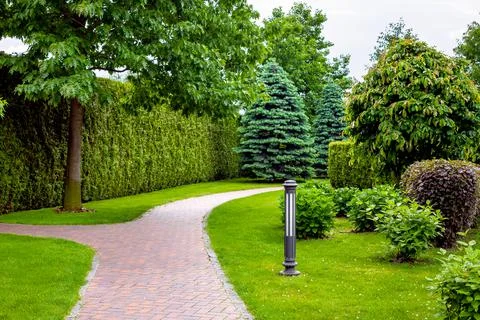 Stone tile footpath curve arcing in the park among green plants. Stock Photos