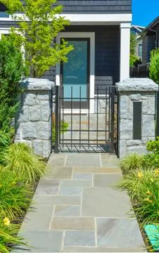 Stone tile paved pathway leading to the entrance door through metal gate Stock Photos