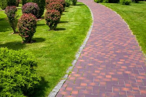 Stone tile pavement curved path in park landscaped with green grass. Stock Photos
