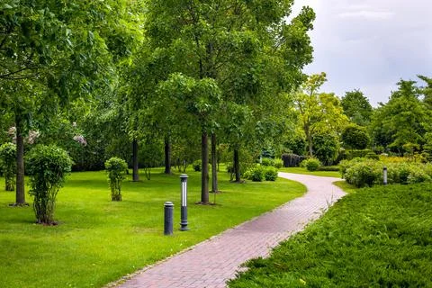 Stone tile walkway curve arcing in the park among green plants. Stock Photos