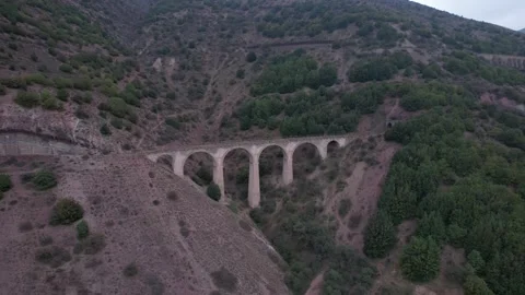 Stone viaduct bridge spans green mountain valley with forested hills and rocky Stock Footage 342703752