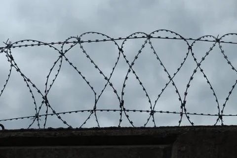 Stone wall with barbed wire against blue sky Stock Photos